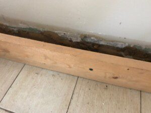 A rotten wall with a wooden floor and some dirt